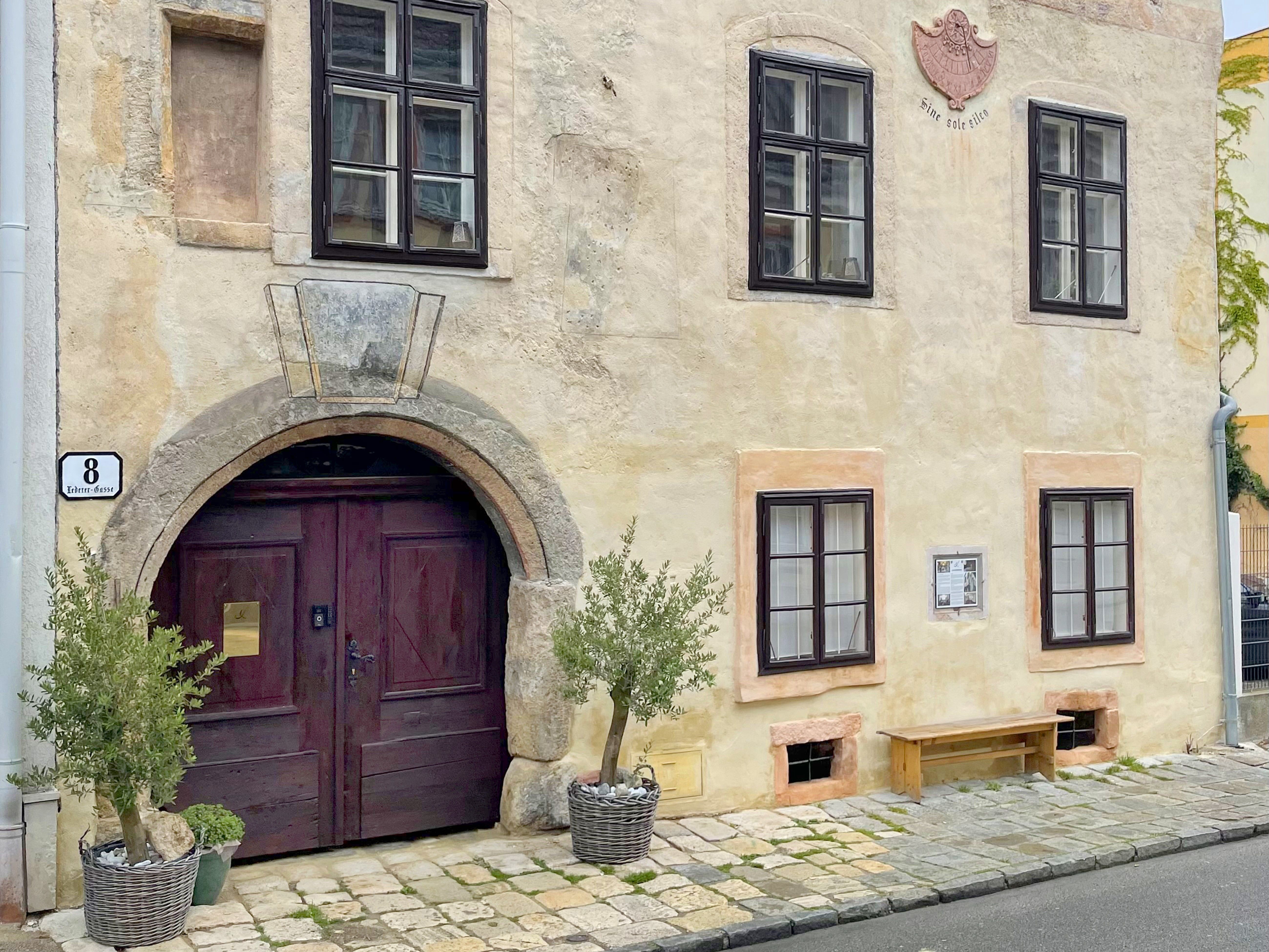Historische Hausfassade mit Holztor und Fenstern, dekoriert mit Pflanzen in Körben.