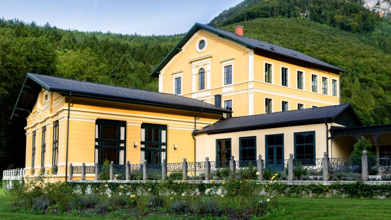 Thalhof Außenansicht, © Thalhof, Katrin Nusterer Außenansicht eines gelben Gebäudes mit Garten und Wald im Hintergrund.