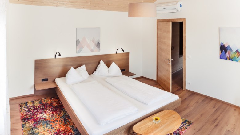 Modernes Schlafzimmer mit Doppelbett, Holzmöbeln und buntem Teppich.
