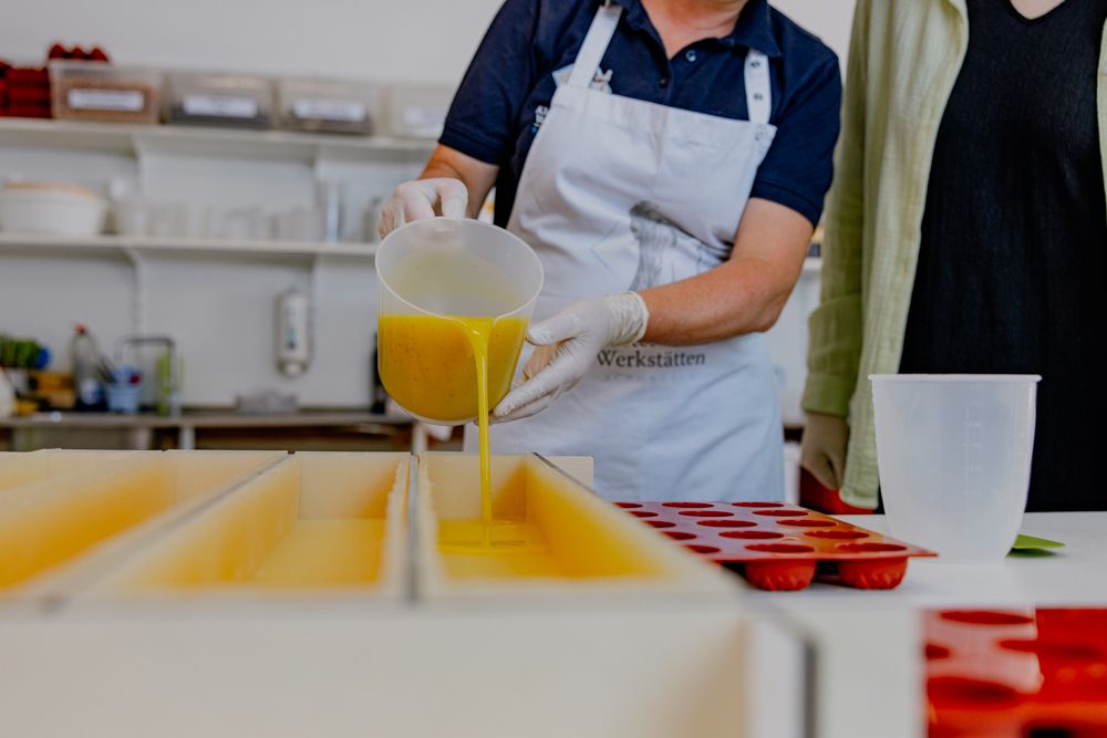 Person gießt gelbe Seife in rechteckige Formen in einer Werkstatt.