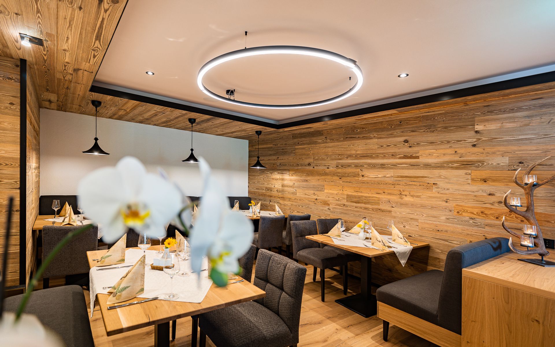 Gemütliches Restaurant mit Holzwänden, modernen Leuchten und elegant gedeckten Tischen.