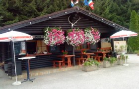 Holzhütte mit Blumen und Sonnenschirmen vor einem Wald.