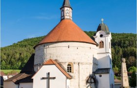 Pfarrkirche Scheiblingkirchen mit rundem Turm und rotem Dach vor blauem Himmel.