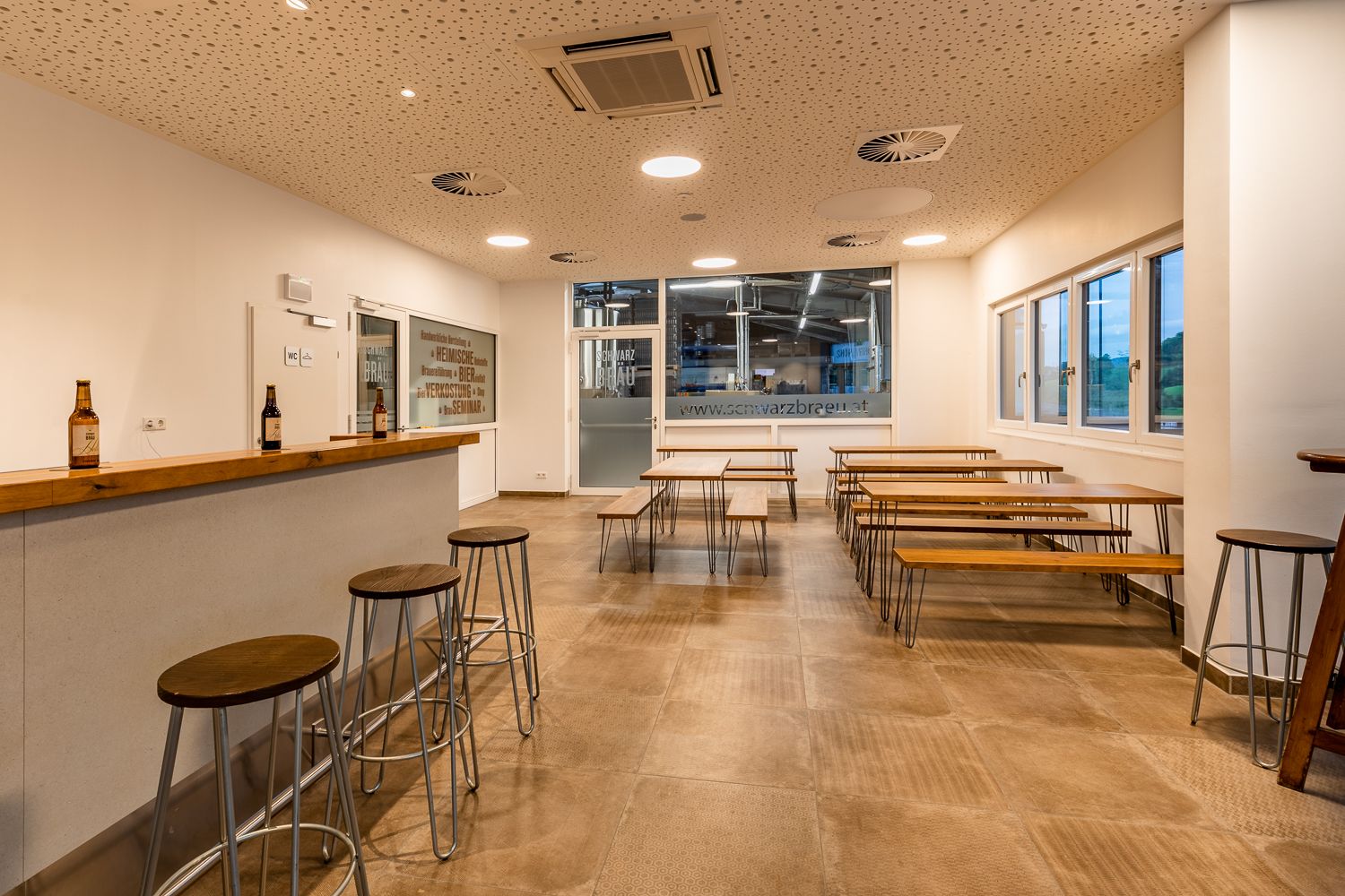 Verkostungsraum einer Brauerei mit Holztischen und -bänken und einer Bar mit Hockern.