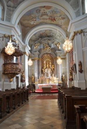 Innenansicht einer barocken Kirche mit Altar, Kanzel und Kronleuchtern.