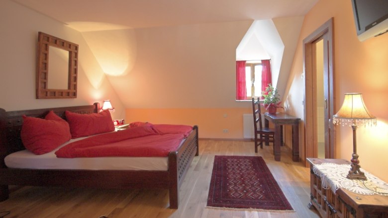 Gem&uuml;tliches Schlafzimmer mit Doppelbett, roter Bettw&auml;sche und Holzm&ouml;beln.