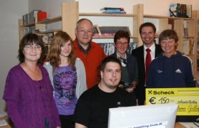 Gruppe von Menschen in einer B&uuml;cherei mit einem Scheck &uuml;ber 150 Euro.