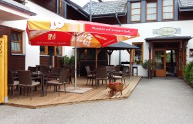 Außenbereich eines Cafés mit Tischen, Stühlen und Sonnenschirmen.