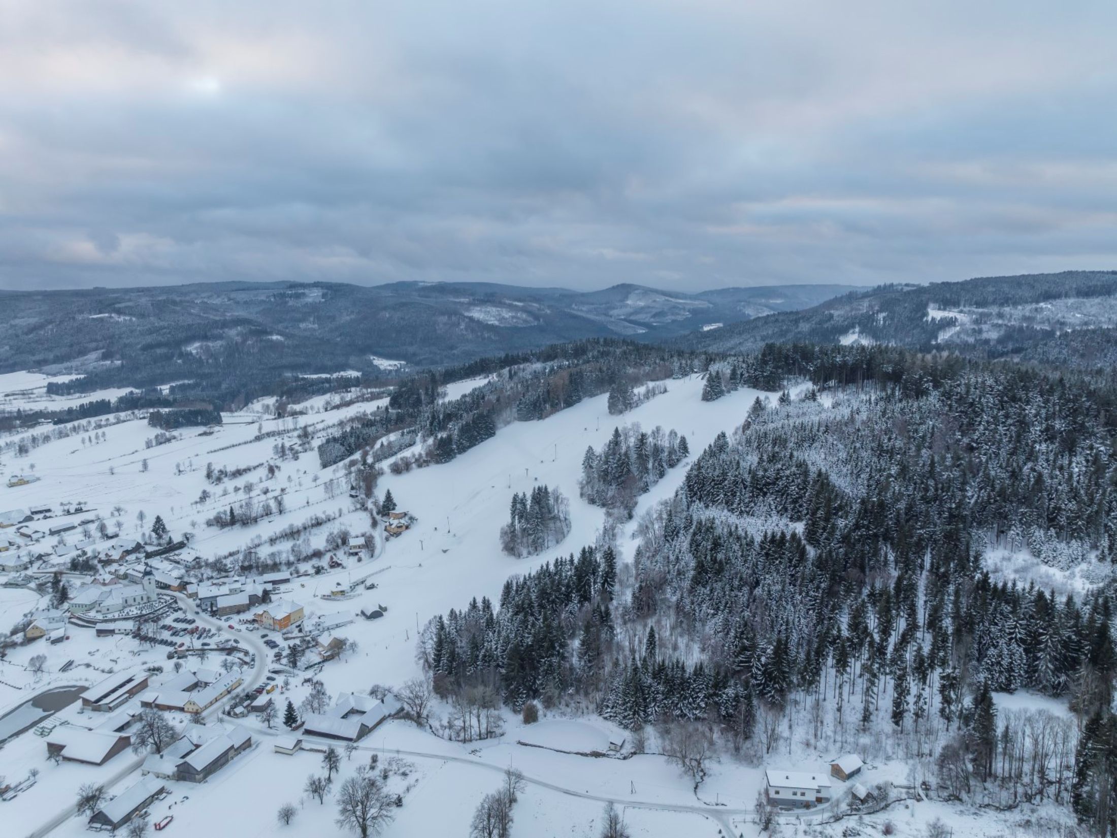 Luftaufnahme einer verschneiten Landschaft mit Hügeln und Wäldern.
