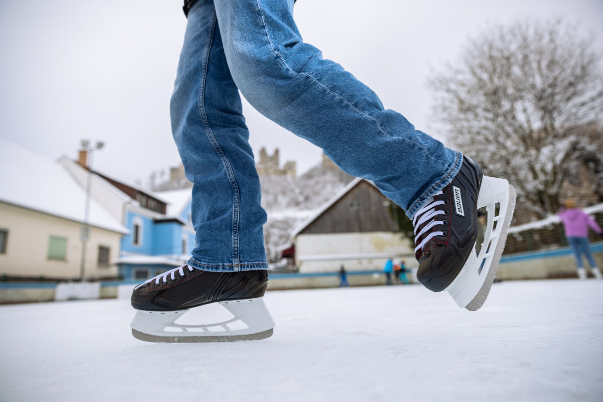 Nahaufnahme von Schlittschuhen auf einer Eisfläche mit Gebäuden und Burgruine im Hintergrund.
