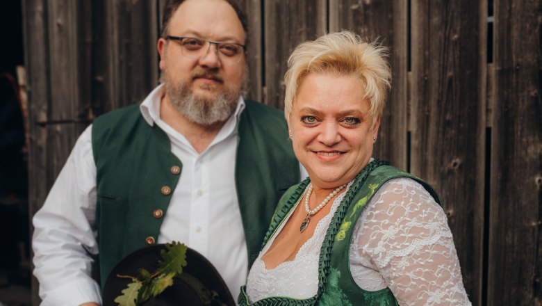 Ein Mann und eine Frau in traditioneller Tracht vor einer Holzwand.