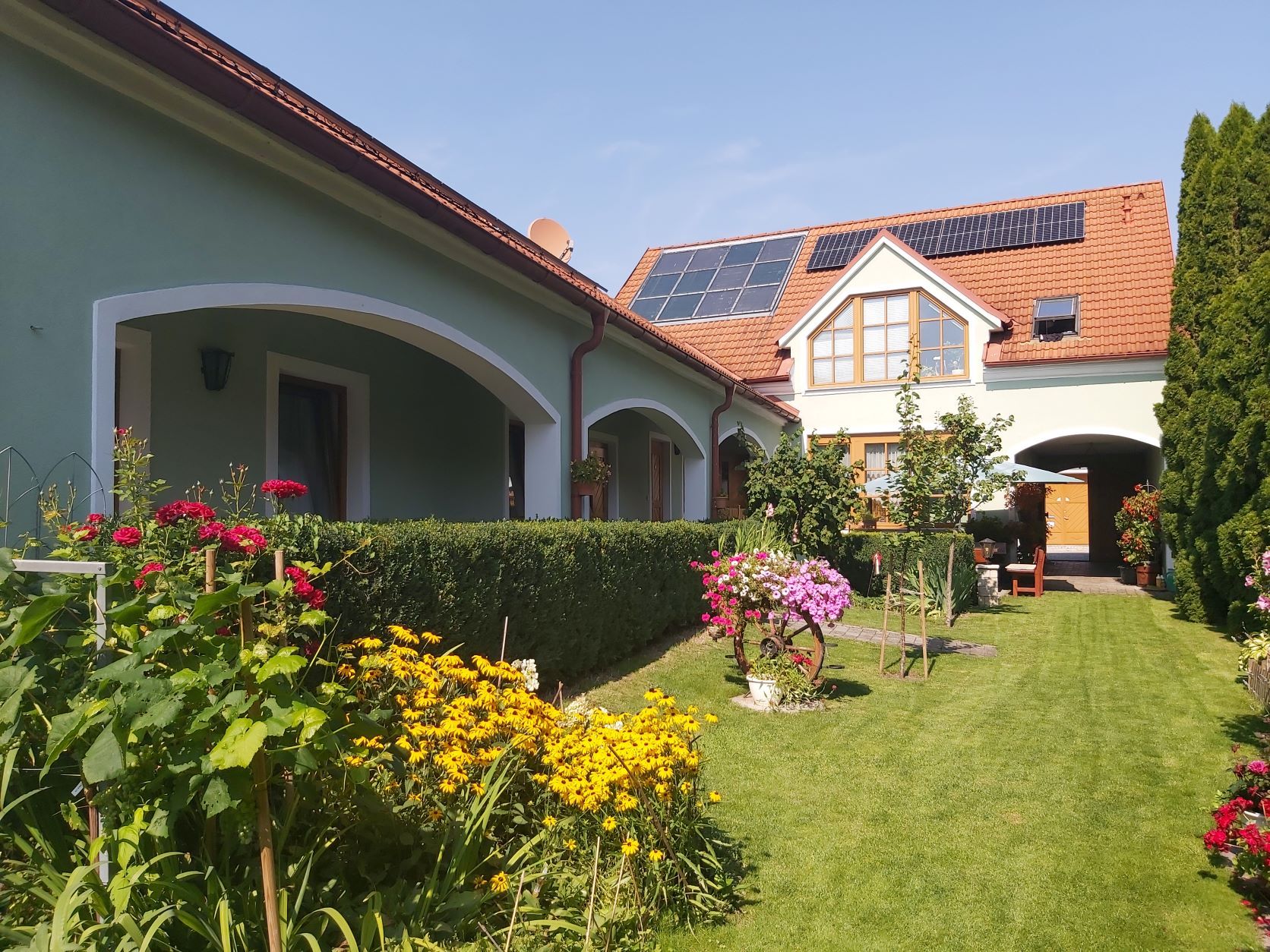 Ein gepflegter Garten mit bunten Blumen und einem Haus mit Solarpanelen auf dem Dach.