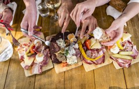 Mehrere H&auml;nde greifen nach Wurst- und K&auml;seplatten auf einem Holztisch.