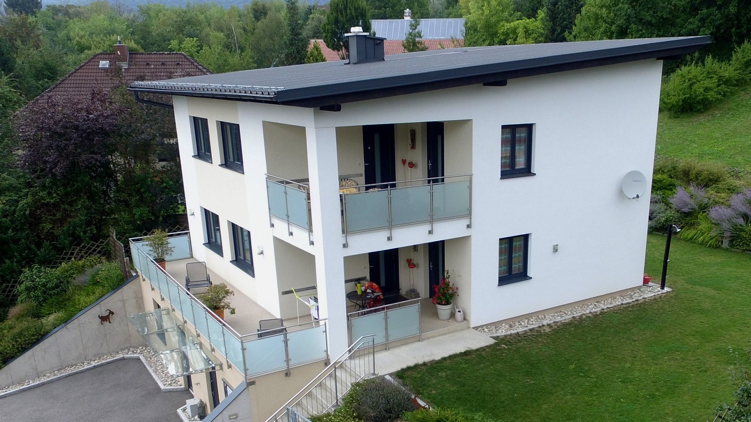 Drohnenaufnahme eines modernen zweistöckigen Hauses mit Balkon und Garten.