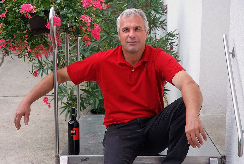 Ein Mann in rotem Hemd sitzt auf einer Treppe neben einer Weinflasche und Blumen.