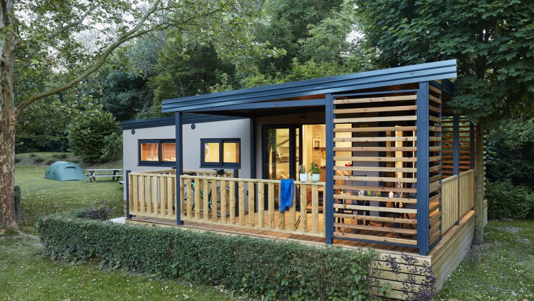 Mobilheim von au&szlig;en mit Blick auf die Terrasse und erleuchtete Zimmer
