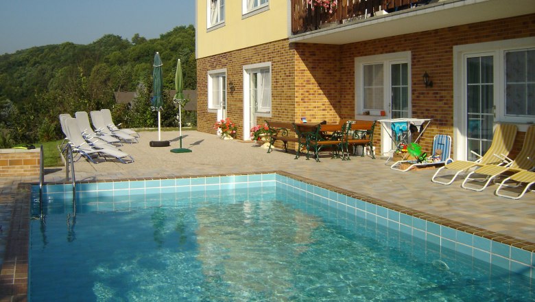 Außenansicht einer Pension mit Pool und Liegestühlen.