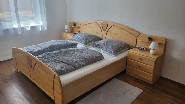 Schlafzimmer mit Doppelbett, Holzm&ouml;beln und grauer Bettw&auml;sche.