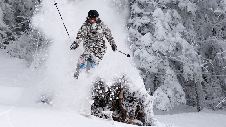 Skifahrer springt durch Pulverschnee im Wald.