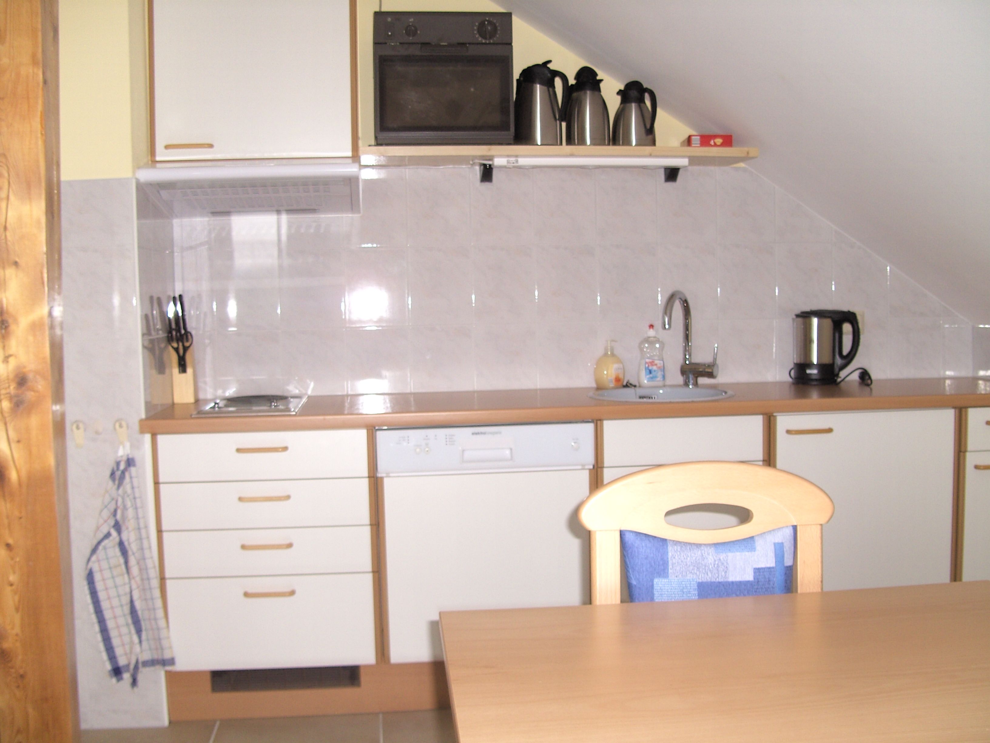 Kleine Küche mit weißen Schränken, Spüle, Wasserkocher und Kaffeemaschinen auf einem Regal.