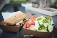 Quinoa-Salat mit Gemüse und Brot in Pappschalen serviert.