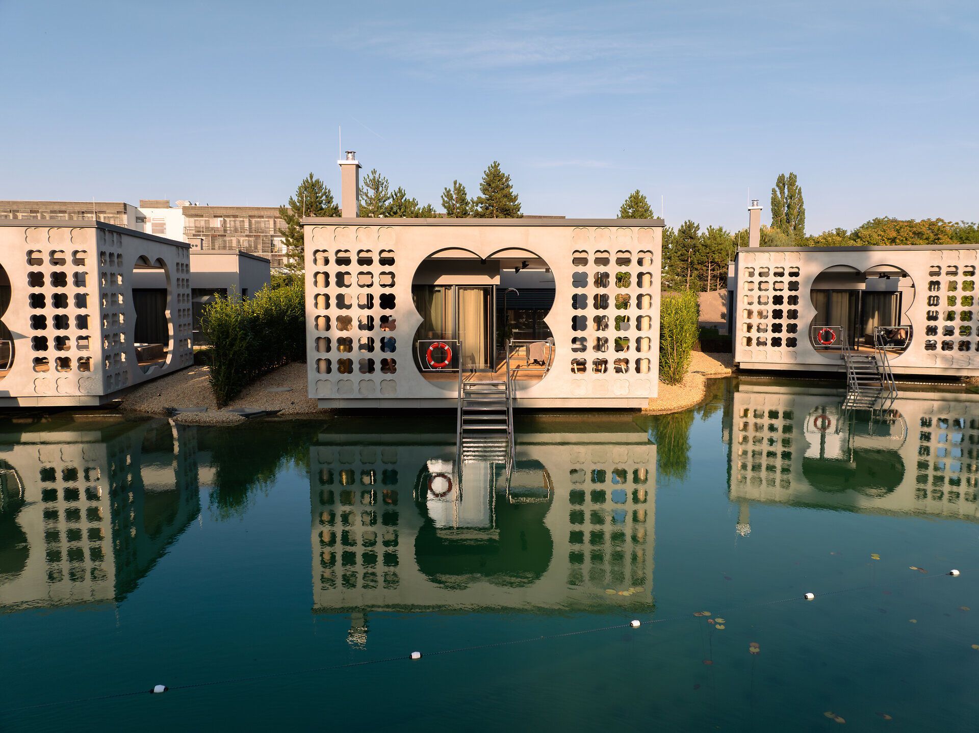 Moderne Villen auf Wasser mit reflektierenden Fassaden und Treppen, umgeben von Natur.