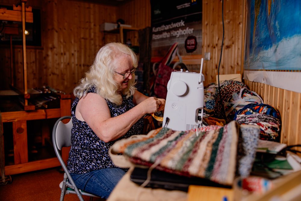 Frau arbeitet an einer Nähmaschine in einem Holzraum.