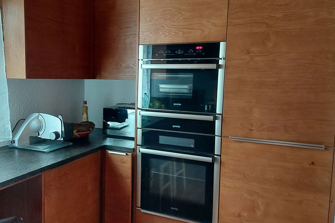Moderne Küche mit Holzschränken, eingebautem Ofen und Arbeitsplatte mit Küchengeräten.