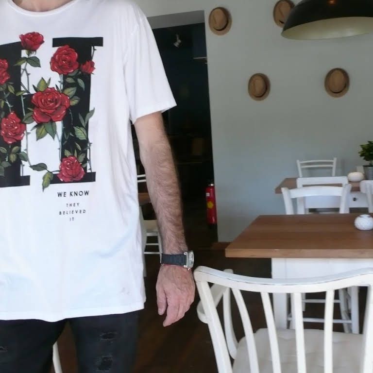 Person in weißem T-Shirt mit Rosenmotiv in einem Café.