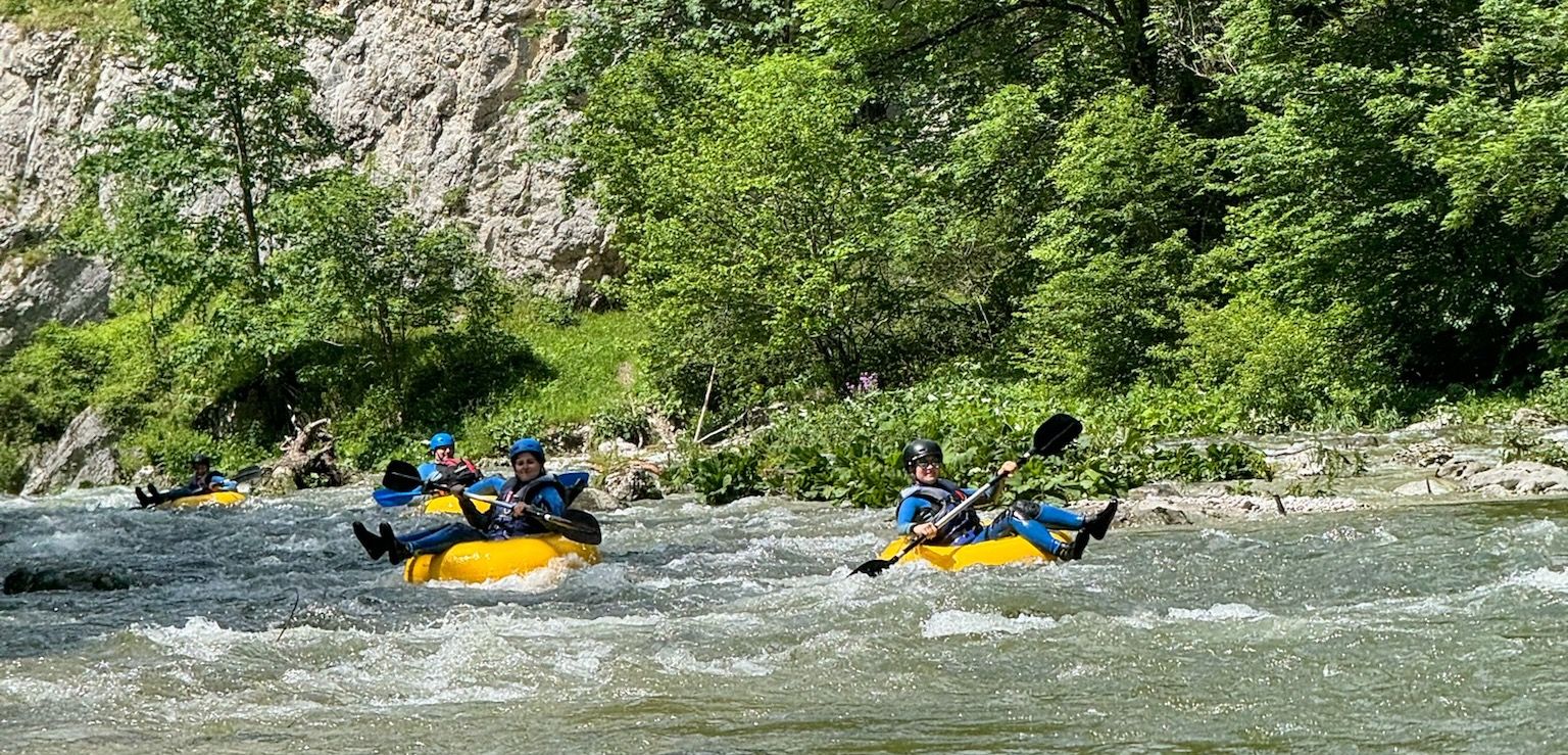 Personen beim Tubing auf einem Fluss in einer grünen, bewaldeten Umgebung.