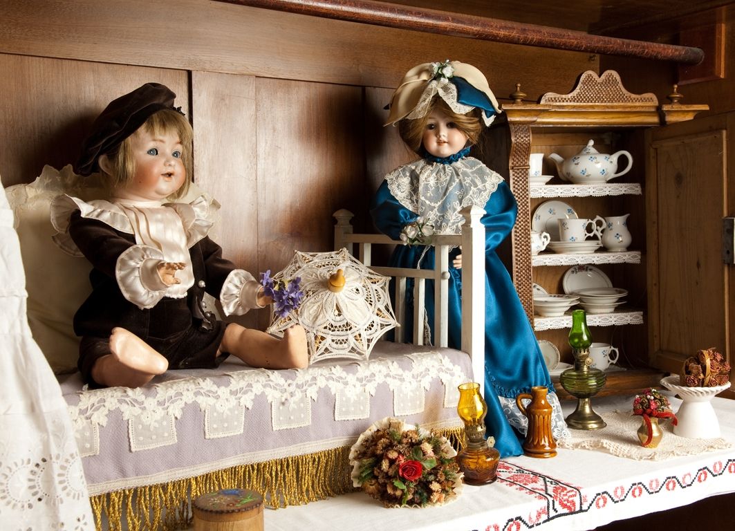 Zwei antike Puppen in einem nostalgischen Raum mit Geschirr und Dekorationen.