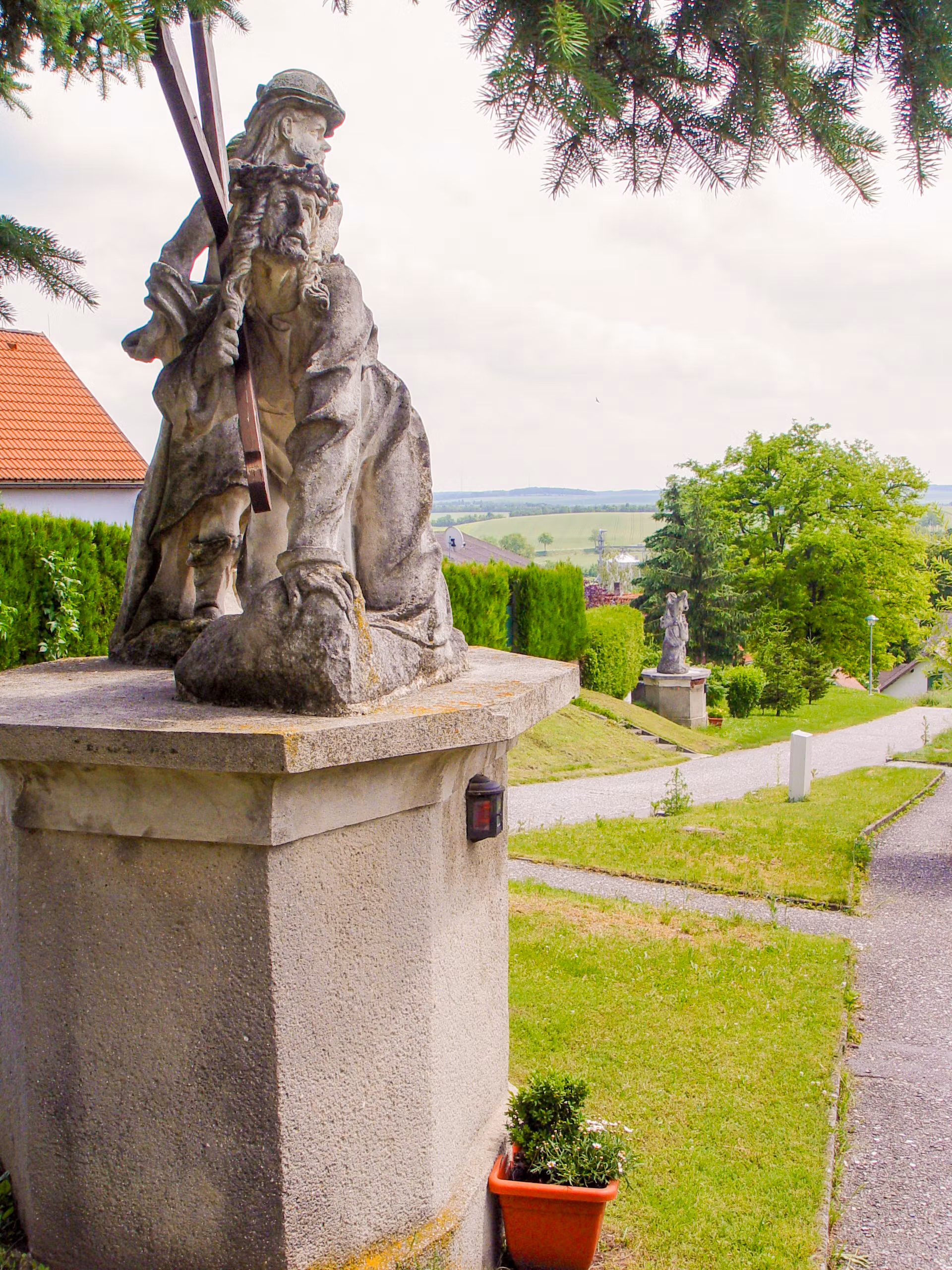 Steinstatue auf einem Sockel mit grüner Landschaft im Hintergrund.