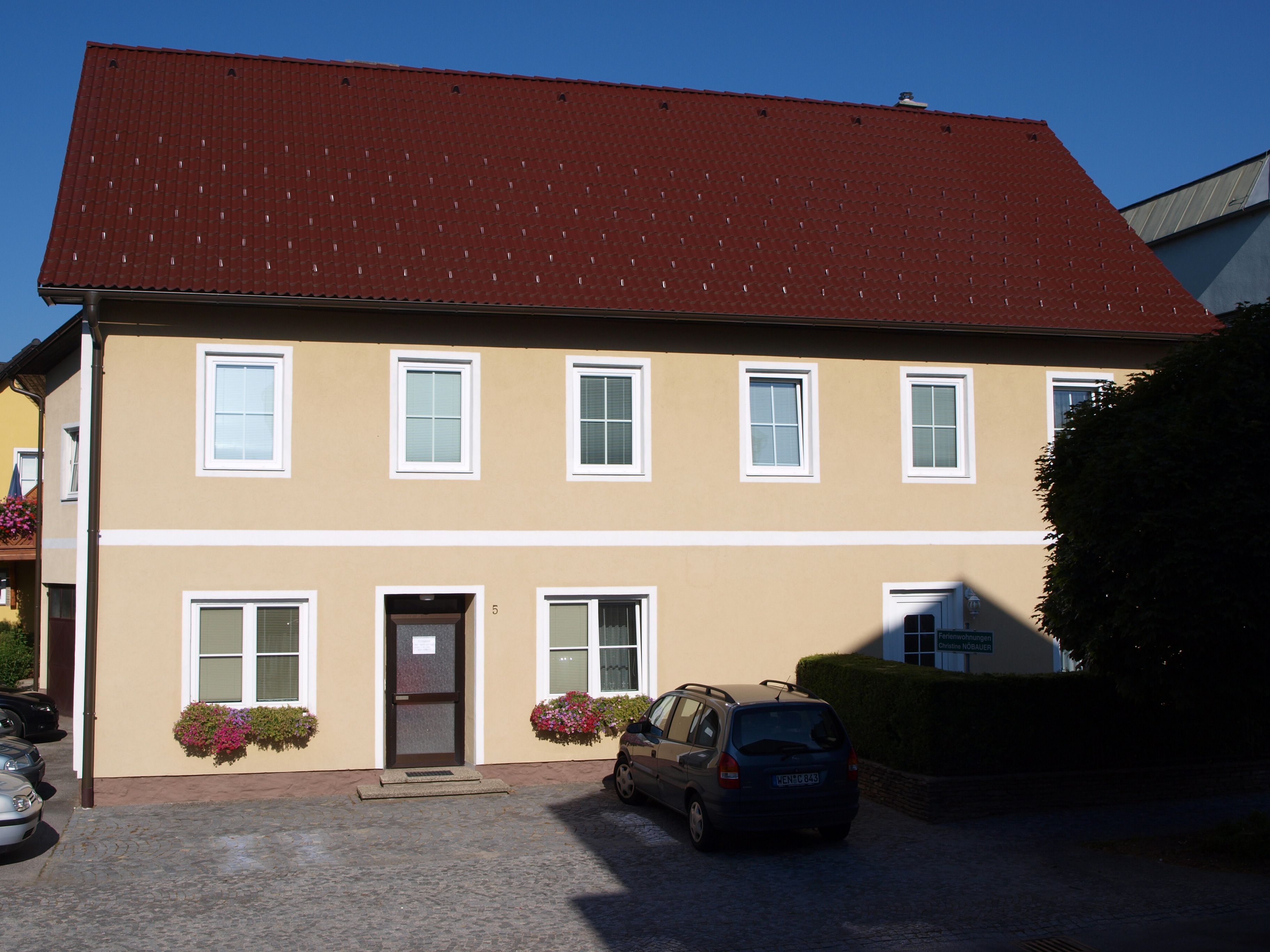 Gelbes zweistöckiges Haus mit rotem Dach und mehreren Fenstern.