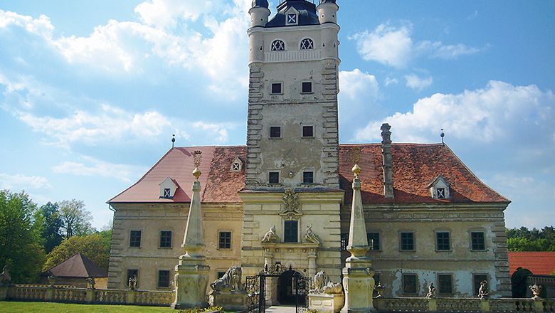Schloss Greillenstein mit Turm und roten Dächern, umgeben von Statuen und einem Tor.