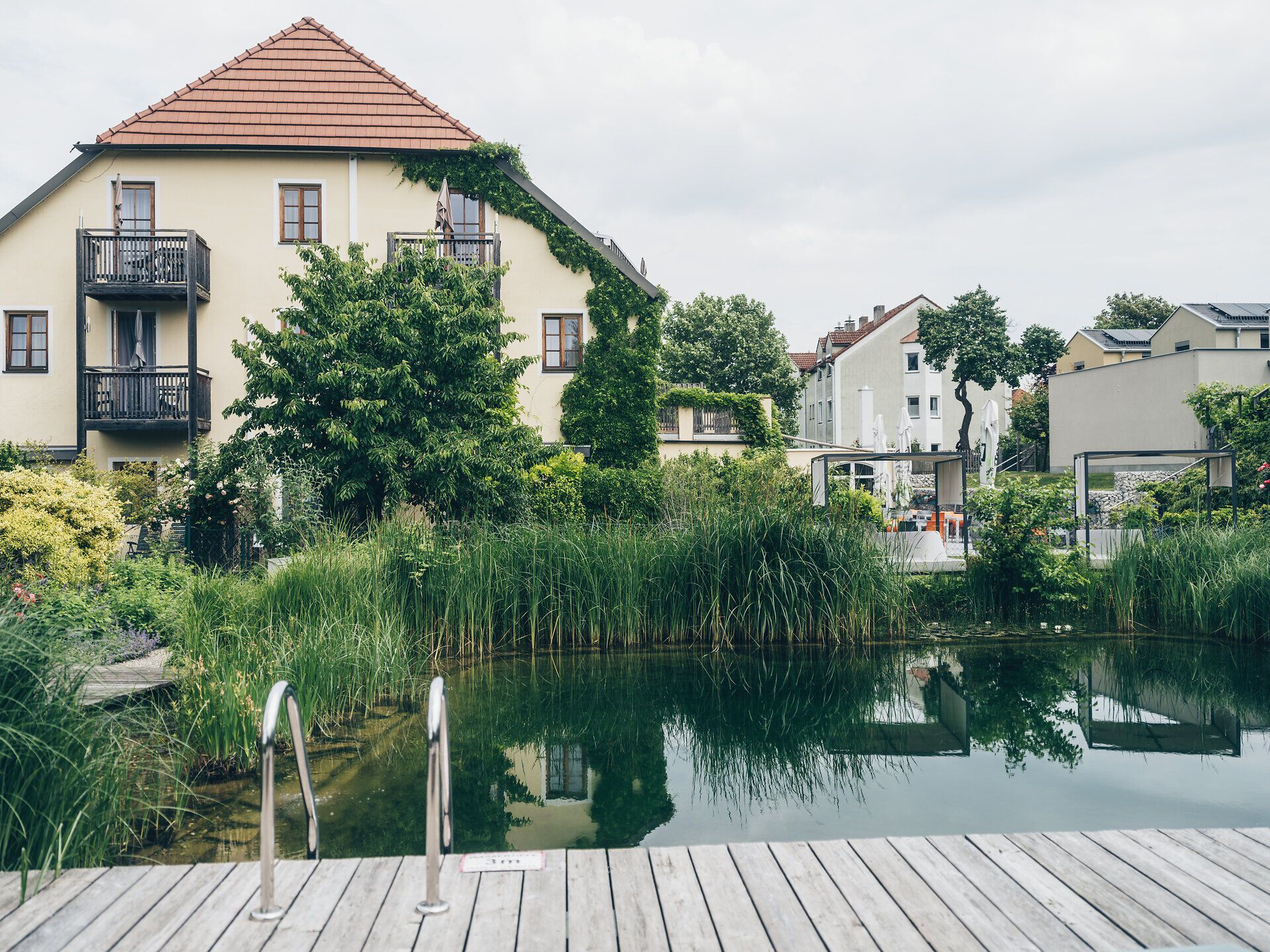 Umgeben von üppigem Grün und sanften Hügeln lädt die ruhige Wasserfläche zum Verweilen ein. Die harmonische Verbindung von Natur und Architektur schafft eine einladende Atmosphäre, die zum Entspannen und Genießen einlädt.