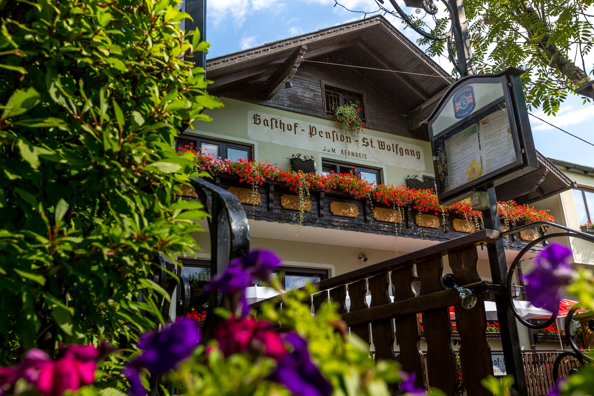 Gasthof Pension St. Wolfgang mit Blumen geschmücktem Balkon und Schild im Vordergrund.