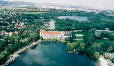 Luftaufnahme von Brunn am Gebirge mit einem großen Gebäude am See und grüner Landschaft.