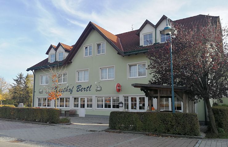 Ein zweistöckiges Gebäude mit der Aufschrift 'Gasthof Bertl', umgeben von Bäumen und Sträuchern.