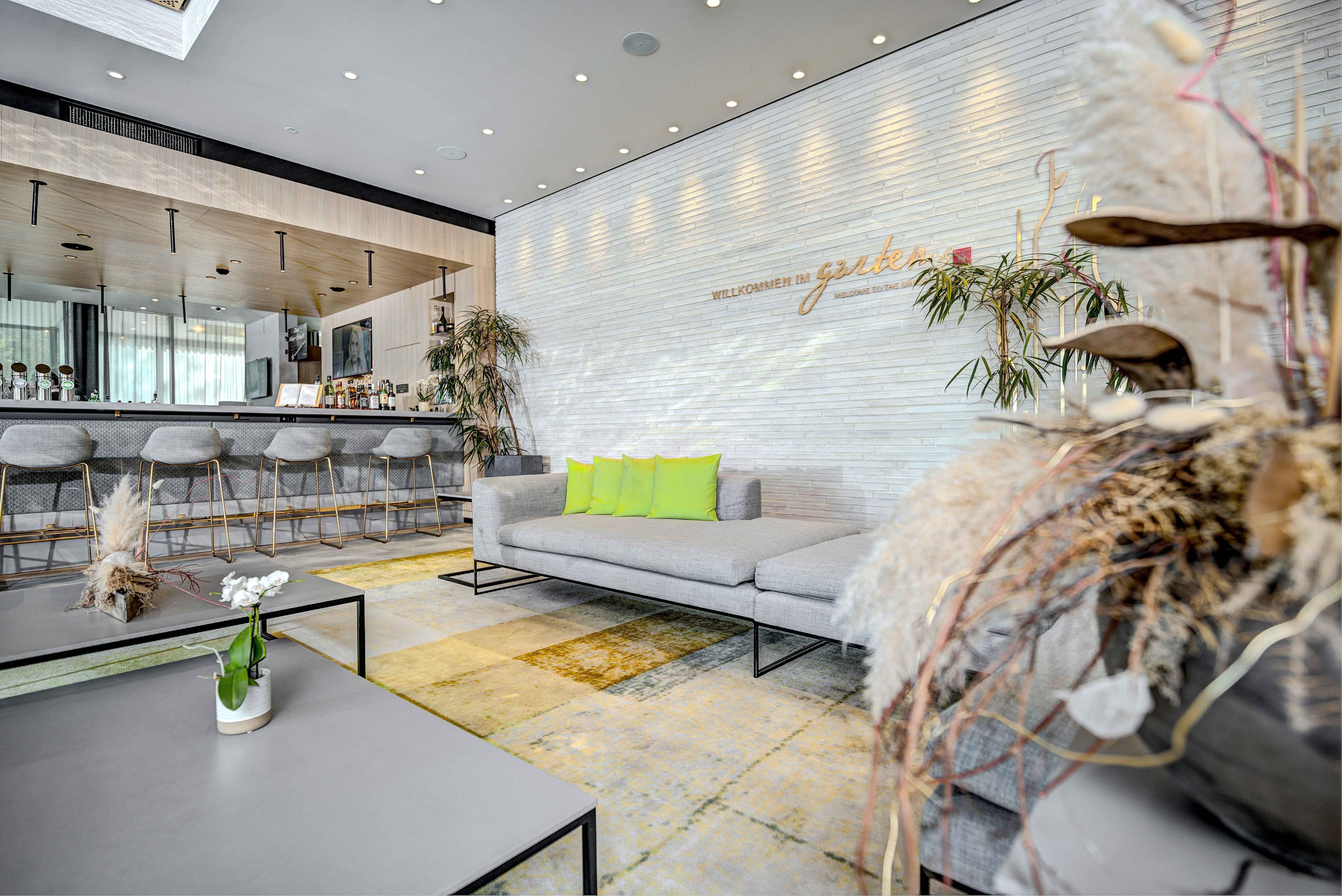 Moderne Hotel-Lobby mit Bar, grauen Sofas und grünen Kissen im Hilton Garden Inn Wiener Neustadt.