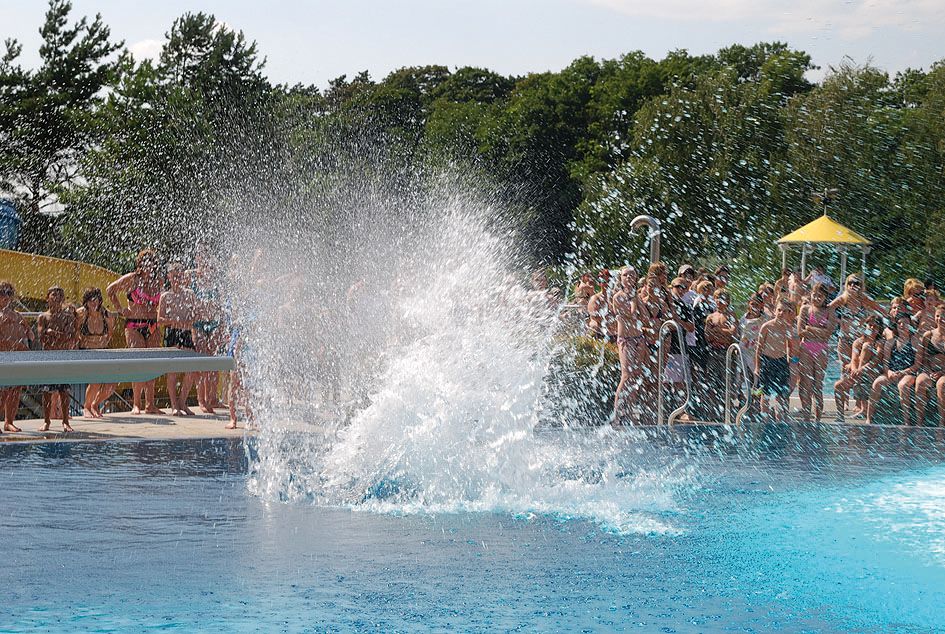 Menschen im Freibad beobachten einen großen Wasserspritzer im Pool.
