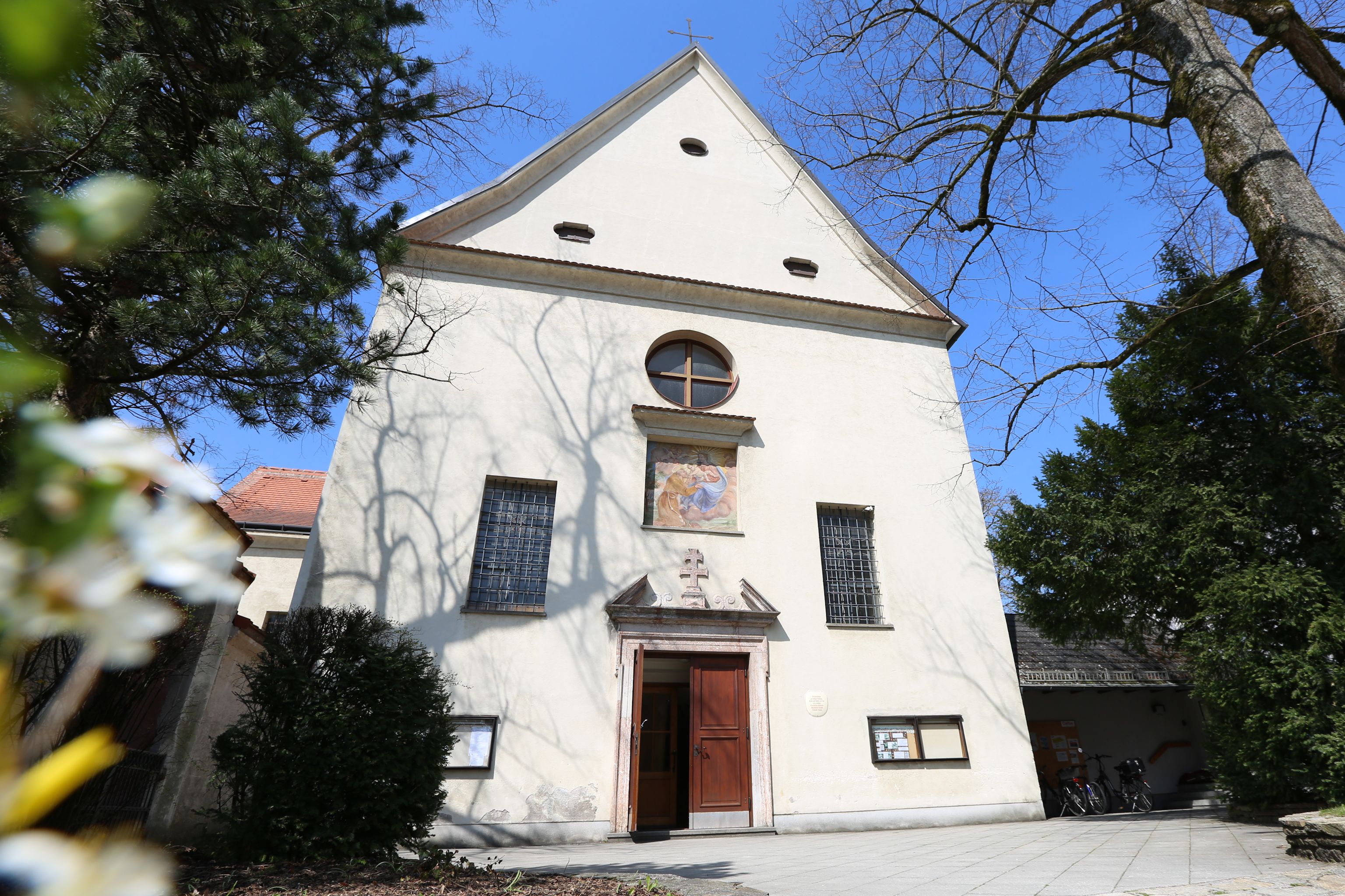 Fassade der Kapuzinerkirche mit Eingang und Fenstern, umgeben von Bäumen.