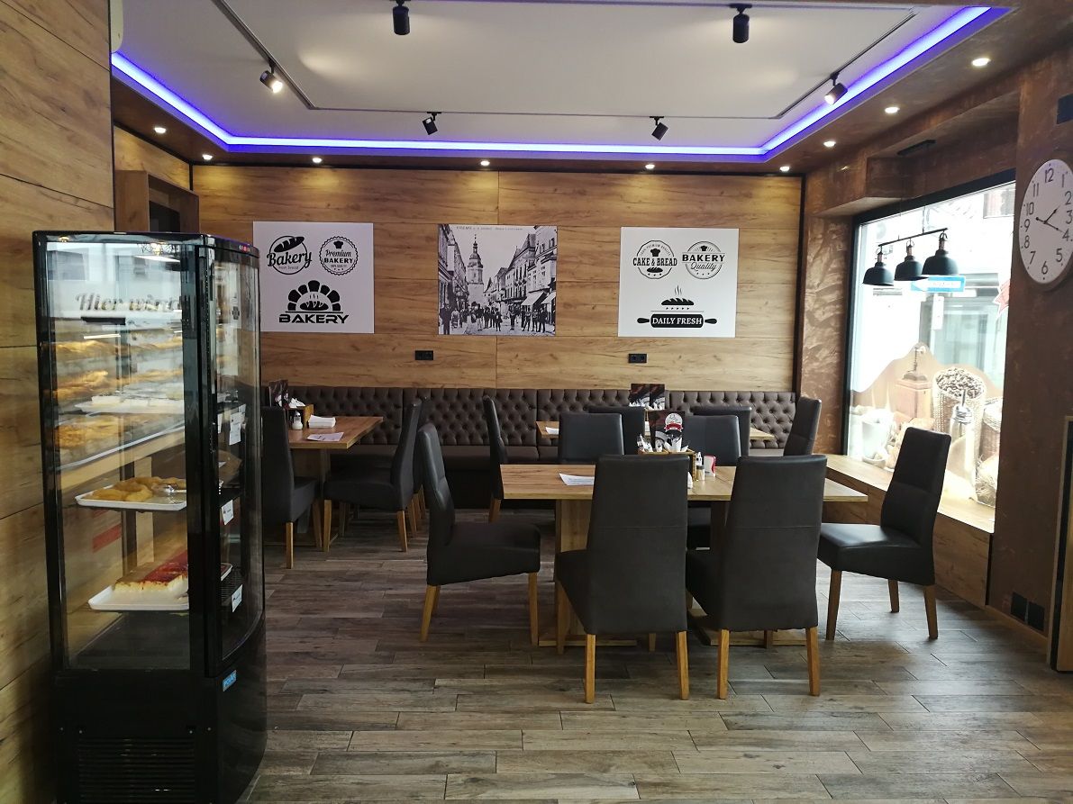 Innenansicht einer modernen Bäckerei mit Holzwänden, Tischen und Stühlen.