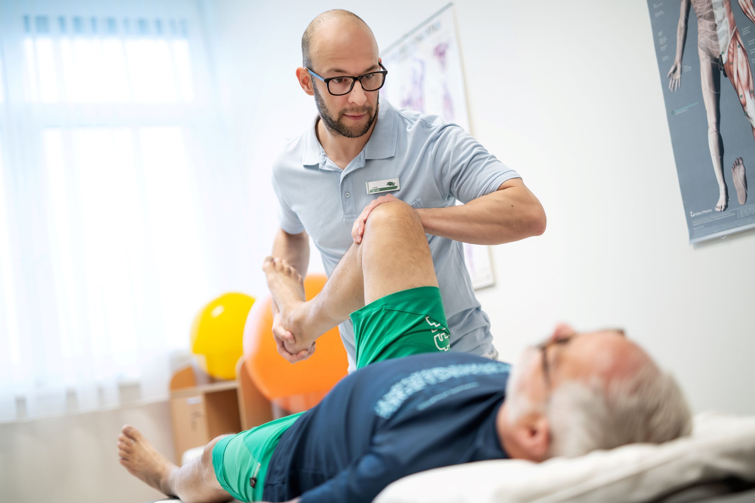 Ein Physiotherapeut behandelt das Bein eines liegenden Patienten in einem Behandlungsraum.