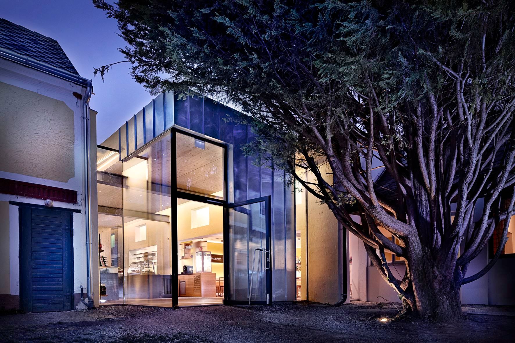 Moderne Glasfassade eines Gebäudes bei Nacht, umgeben von Bäumen.