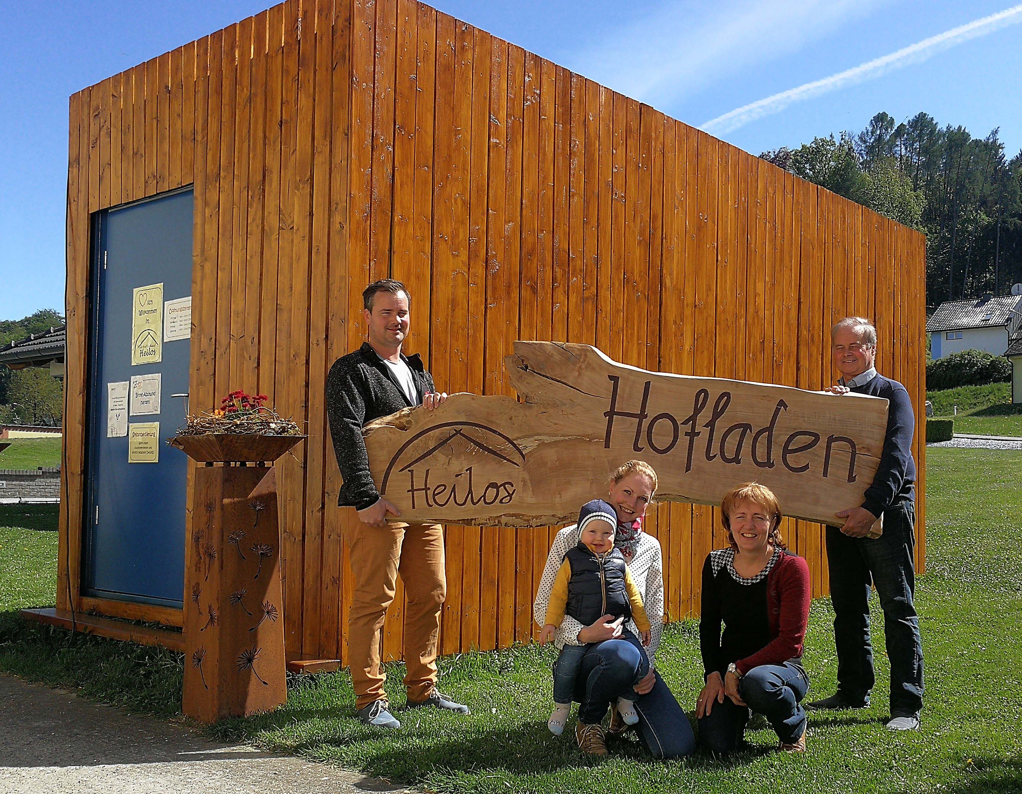 Familie vor einem Holzgebäude mit einem Schild 'Heilos Hofladen'.