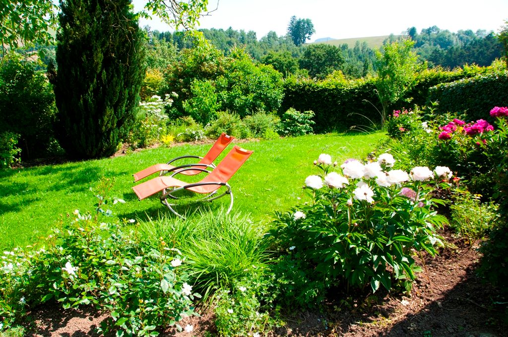 Garten mit zwei roten Liegestühlen und blühenden Blumen.