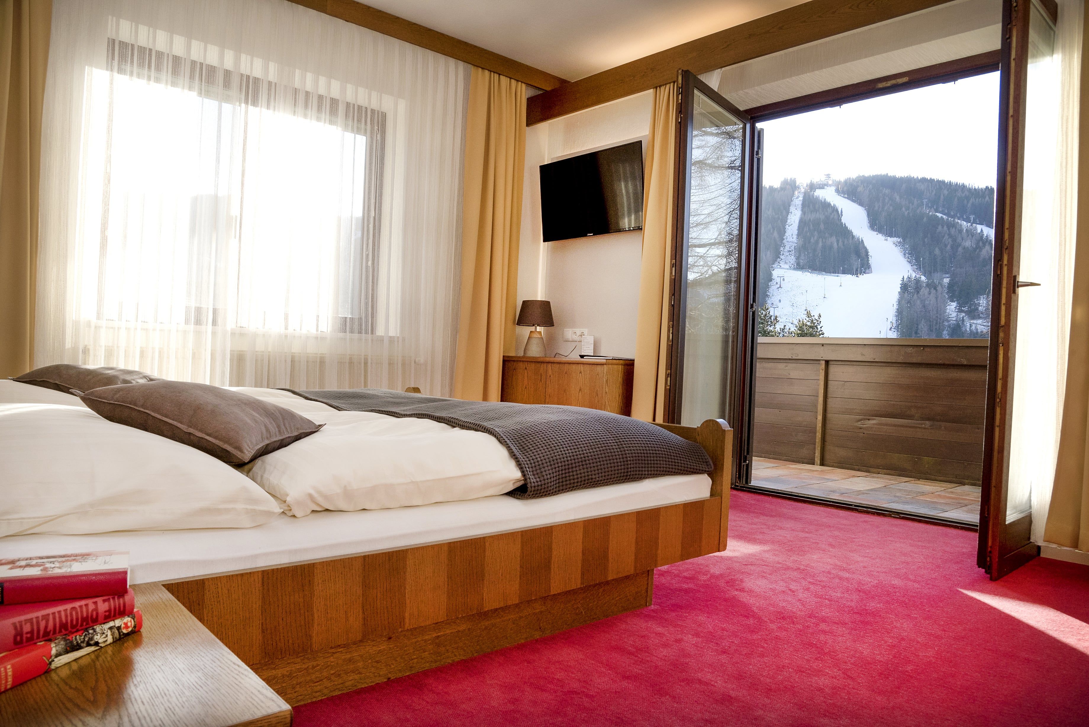 Hotelzimmer mit offenem Balkon und Blick auf eine schneebedeckte Skipiste.