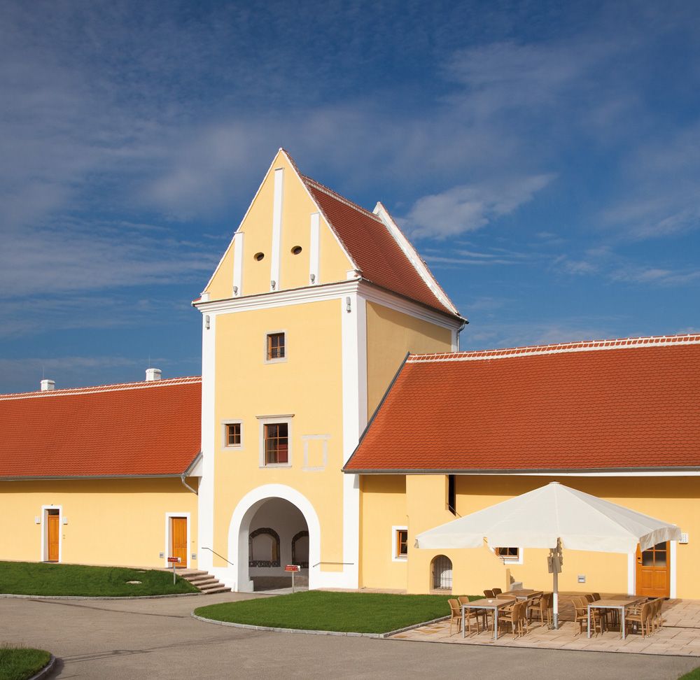 Gelbes Gebäude mit rotem Dach und Torbogen, blauer Himmel im Hintergrund.
