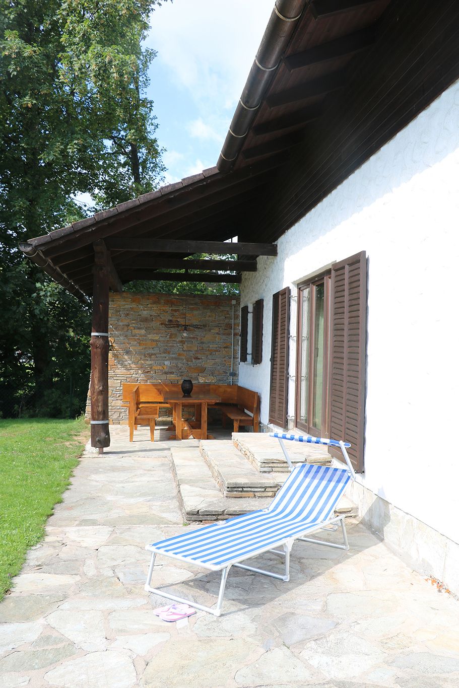 Terrasse mit Liege und Holzmöbeln neben einem Haus mit Schindeldach.