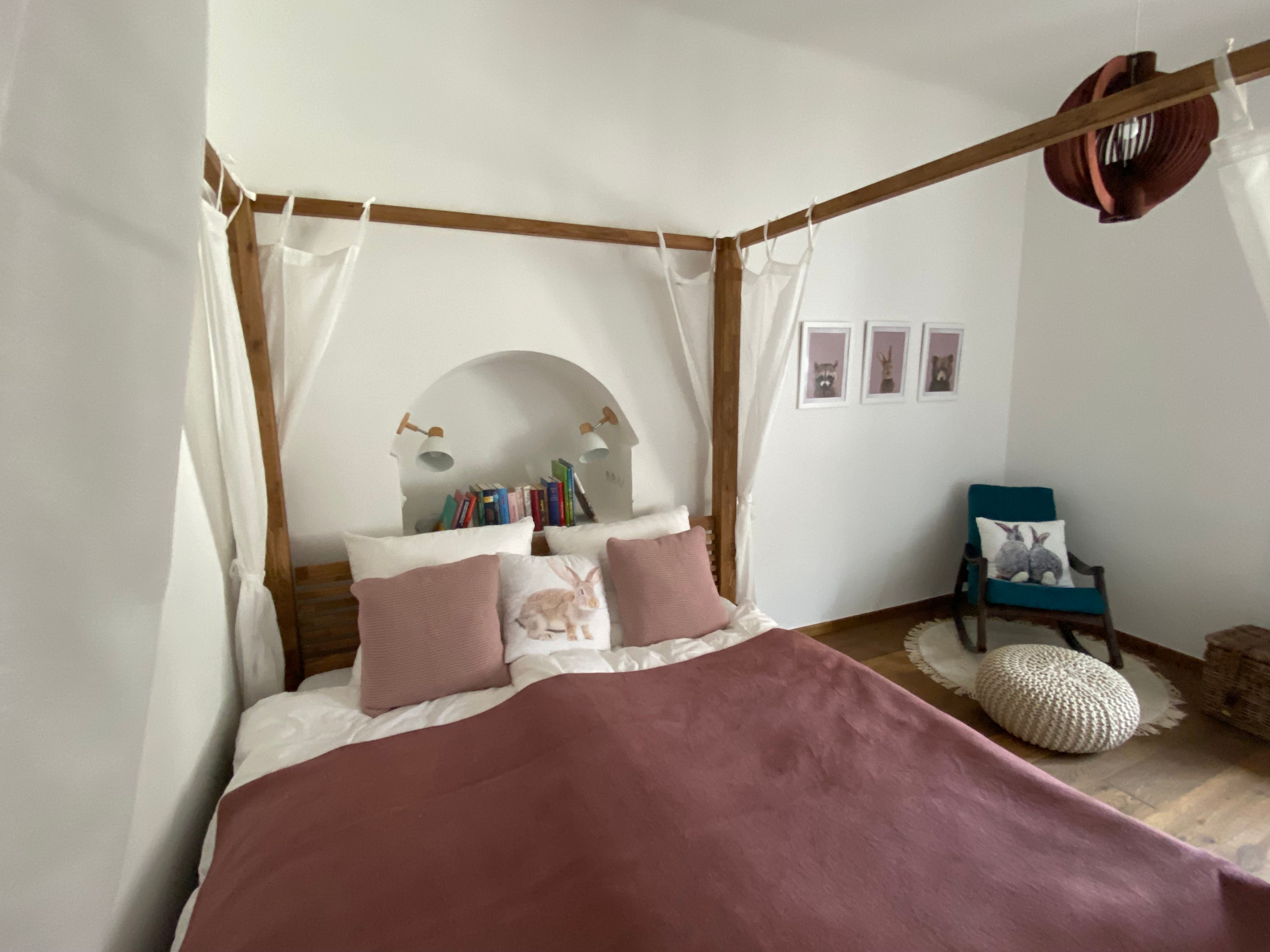 Gemütliches Schlafzimmer mit Himmelbett, Kissen, Büchern und einem Sessel mit Hasenkissen.